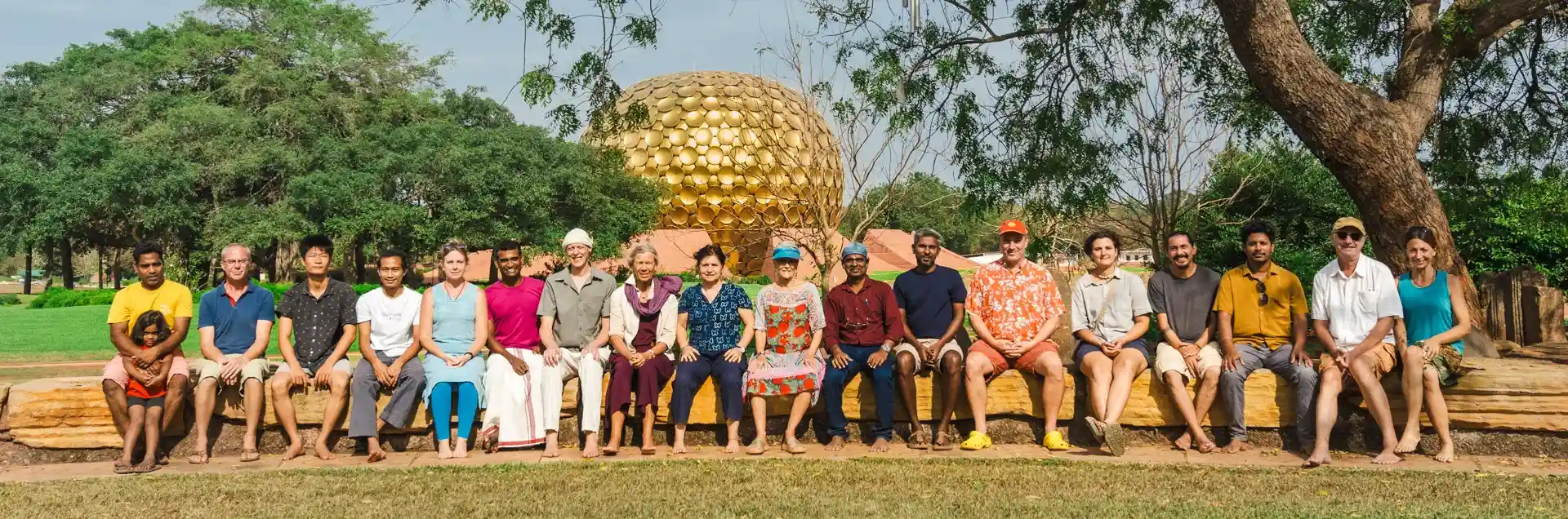 A group of Aurovilians with Matthew Andrews sitting in from of the Matrimandir on a bench