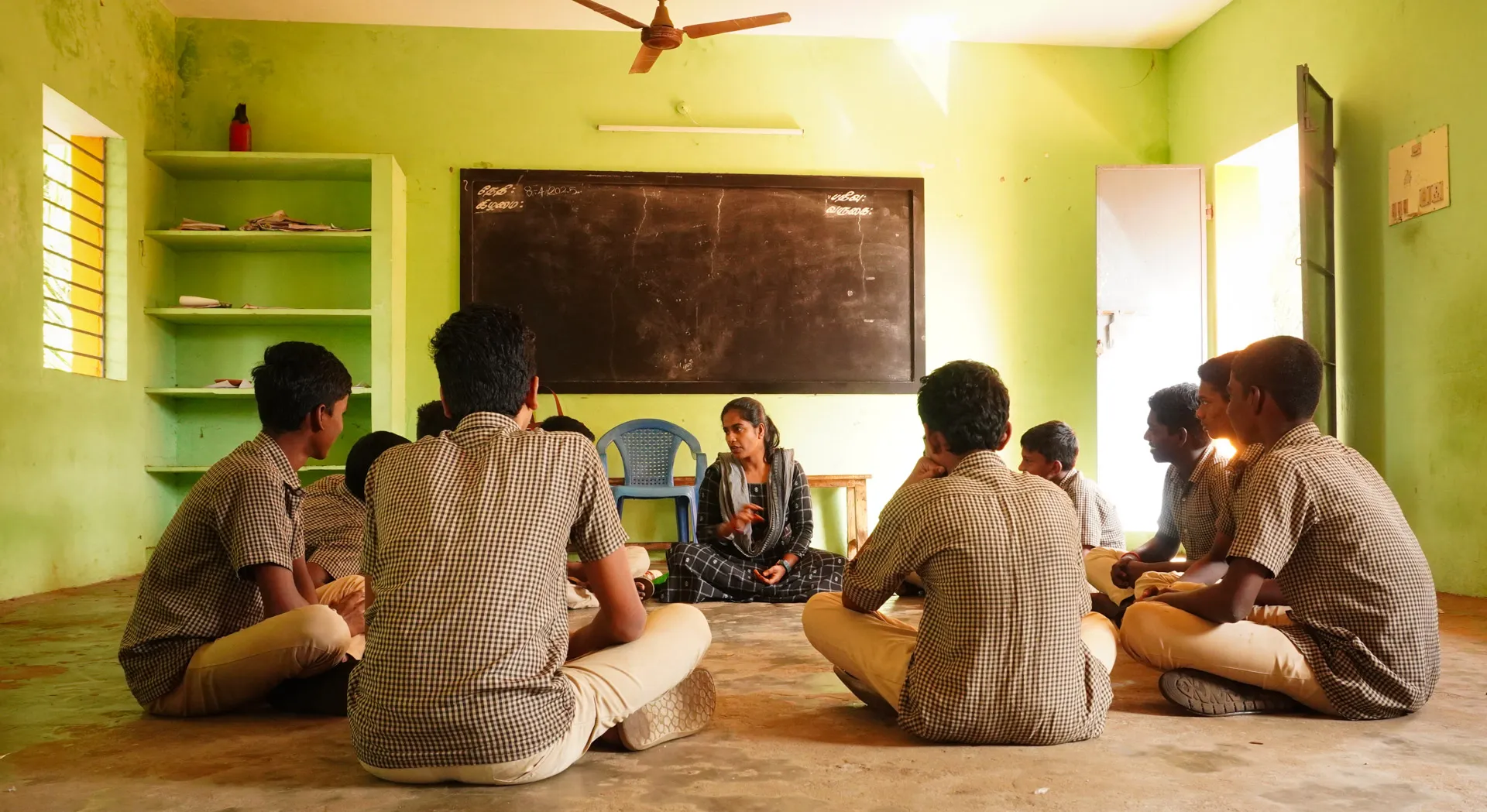 Kalvi in teaching a group of boys with her backs to her