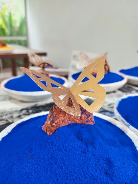 A gold paper butterfly over bowls of blue pigment
