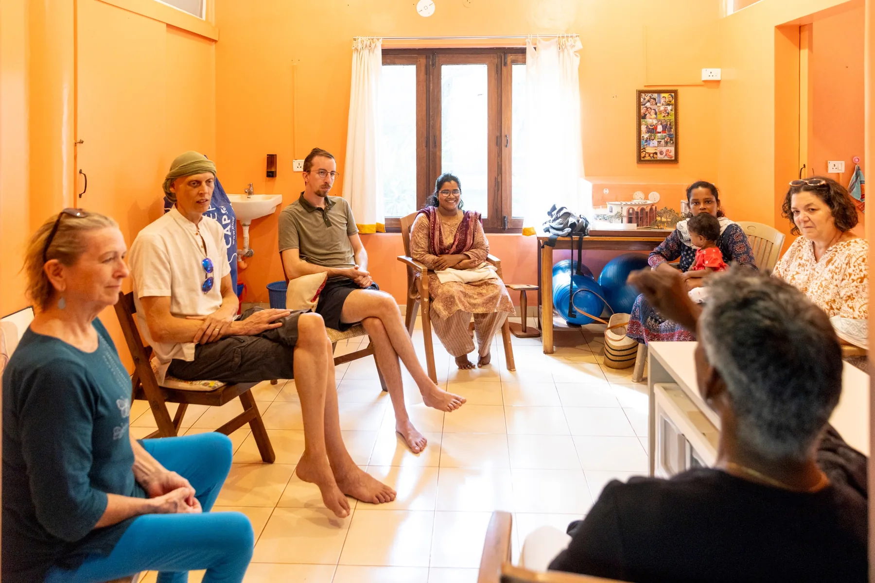 Visitors and team members sitting in a circle in an orange room, with a mother holding her baby