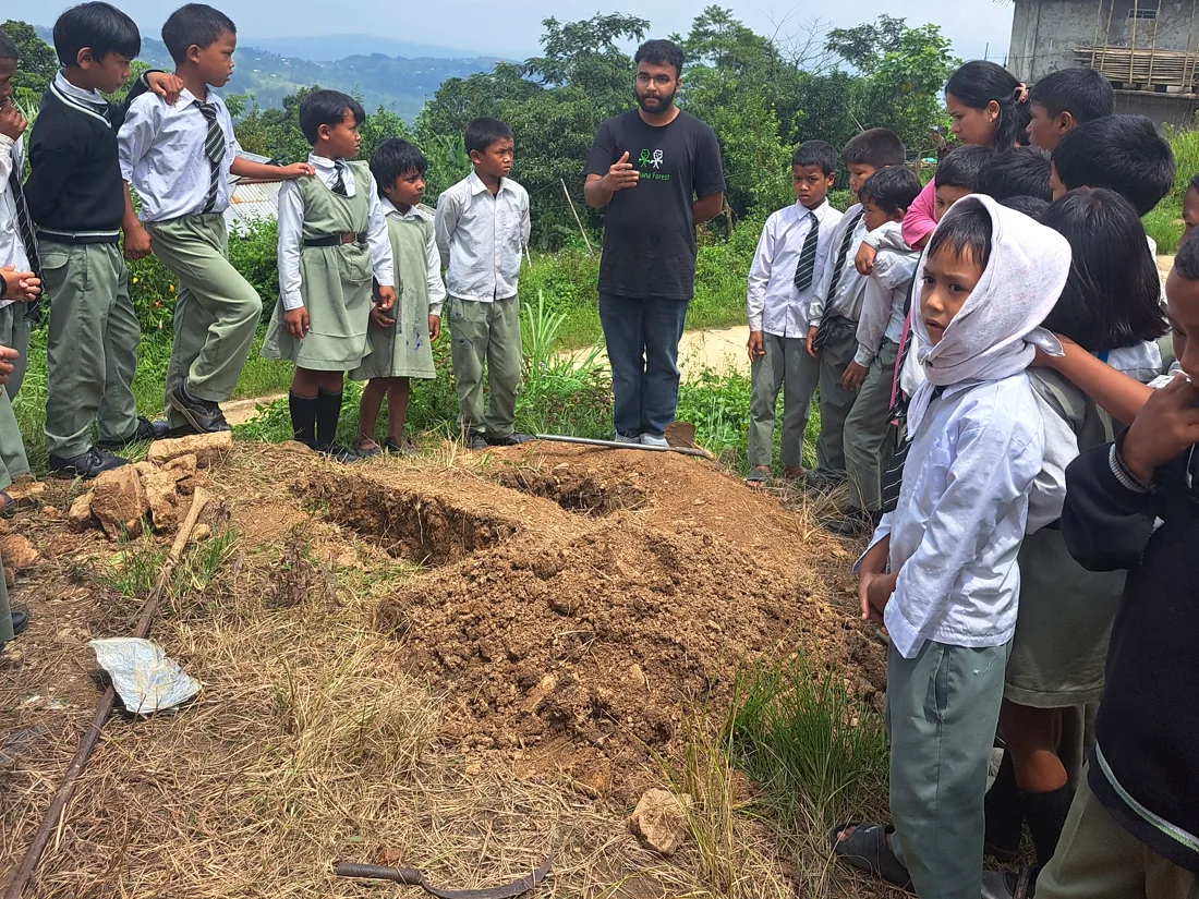 Soham teaching schoolchildren beside a planting pit